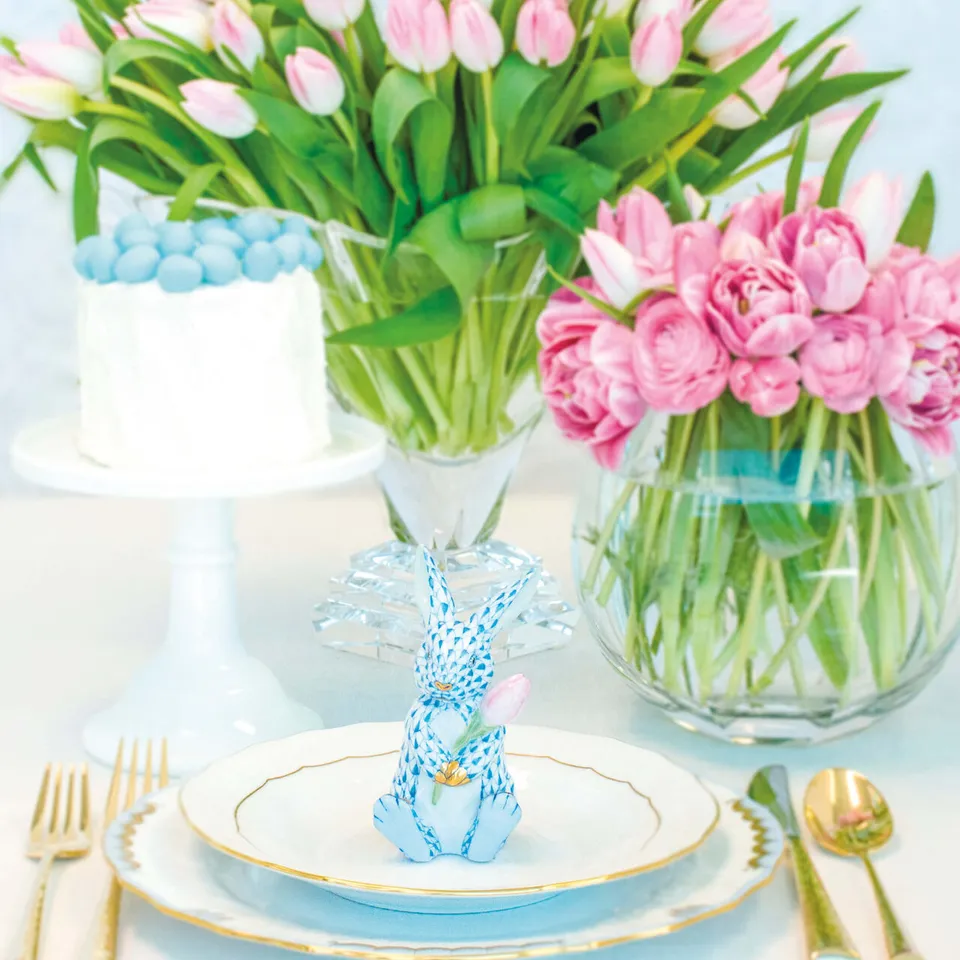 Blue-and-white porcelain bunny at a gold-rimmed place setting surrounded by pink tulips, crystal, and gold flatware