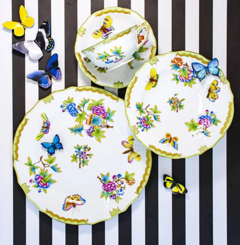 Butterfly-patterned china plates and teacup arranged with colorful butterfly decorations on black-and-white stripes